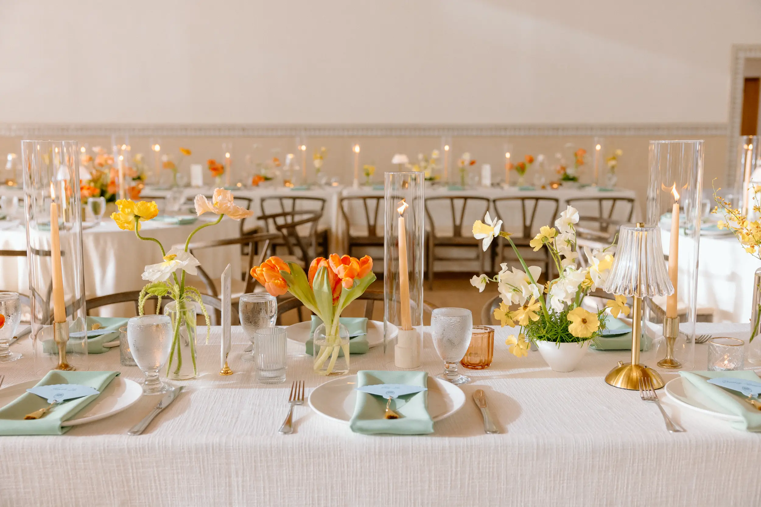 Orange and teal florals and details decorate the tops of every wedding reception table inside Grand Gimeno.