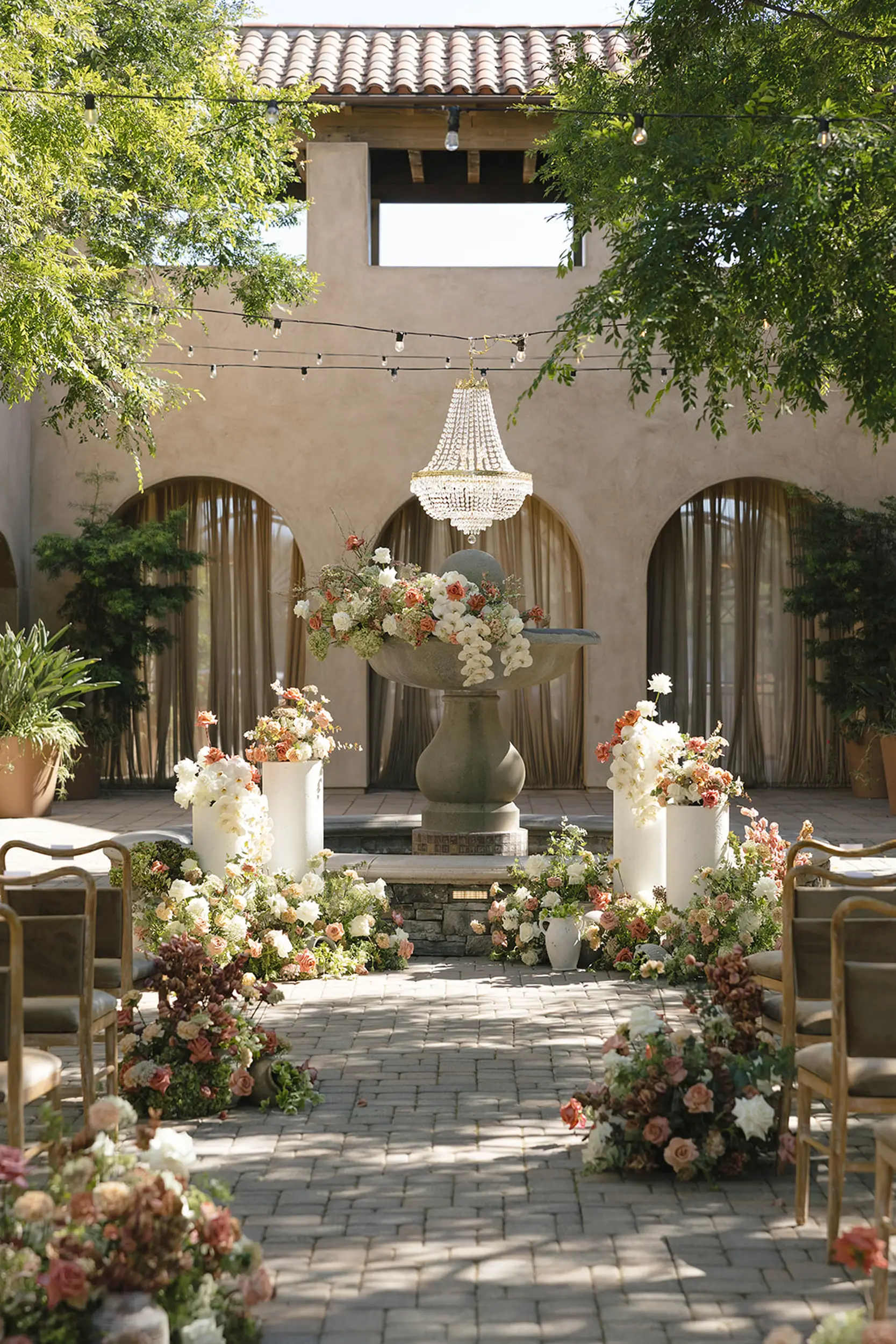 Blush and terracotta florals and pottery decorate the outdoor courtyard for an earthen wedding ceremony with a Spanish fountain backdrop.