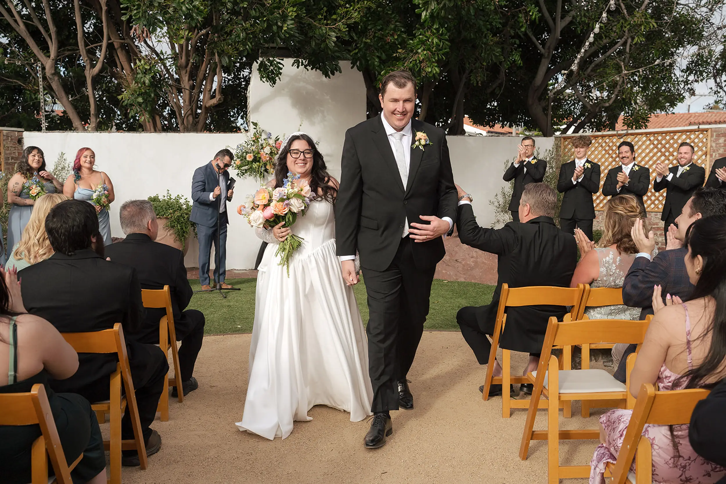 Bride and groom exit their wedding ceremony as guests cheer from their seats.