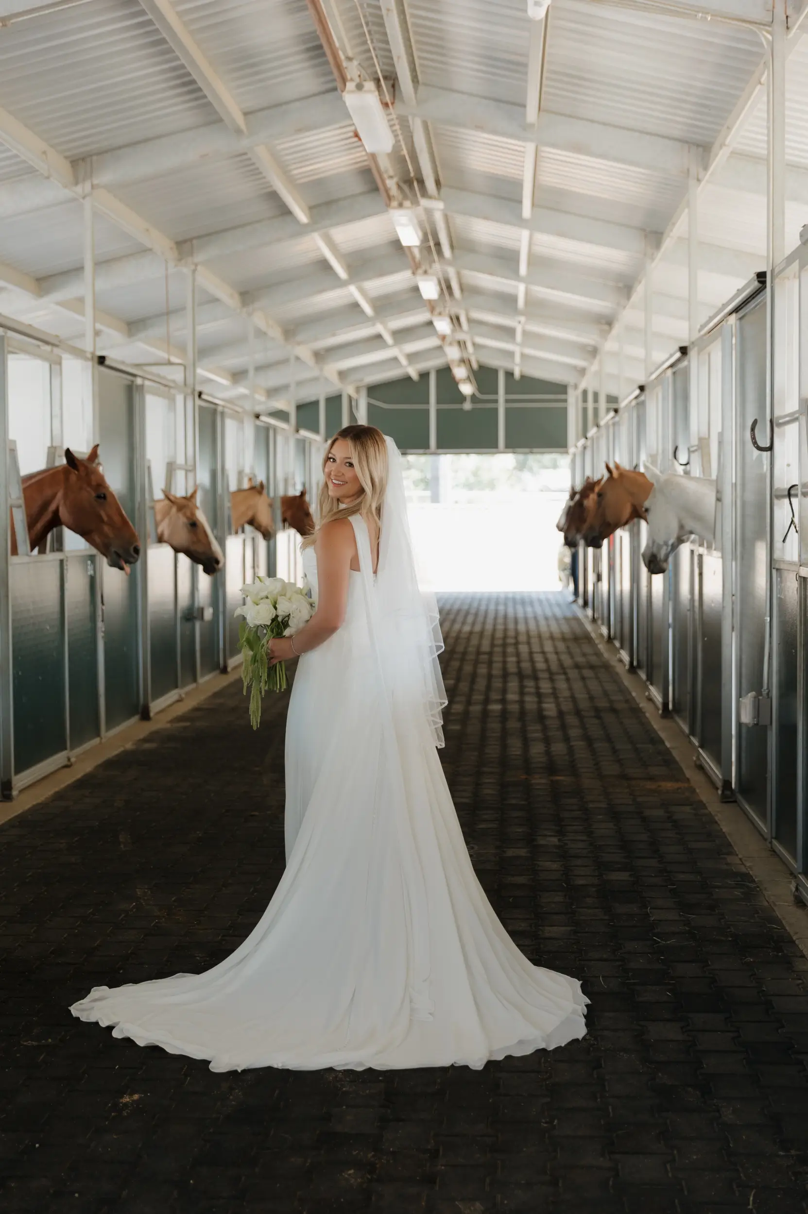 Bride in horse stable posing with the horses before her wedding ceremony.