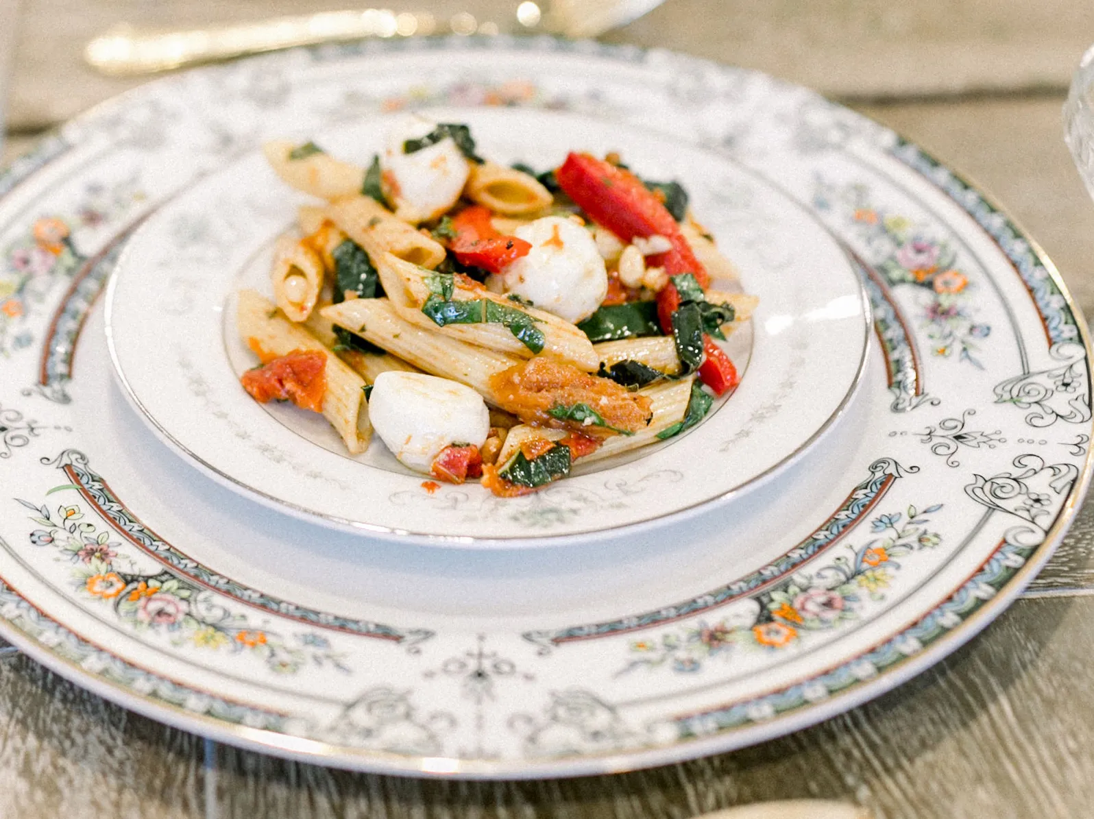 Penne pasta with tomatoes, greens, and mozzarella on a patterned plate.