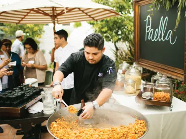 Chef preparing paella at an outdoor catering station.