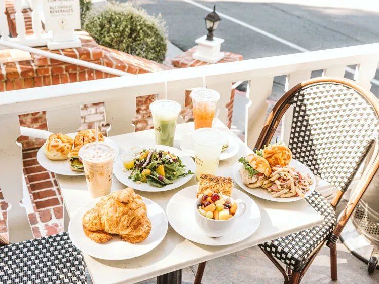 Croissants, sandwiches, salad, fruit, and iced drinks on an outdoor cafe table.