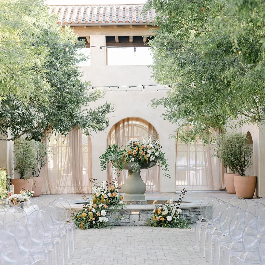 Clear ceremony chairs surrounding a flower-decorated fountain in Serra Plaza's courtyard.
