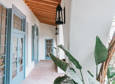 Covered walkway with blue French doors, wooden ceiling and hanging lanterns.