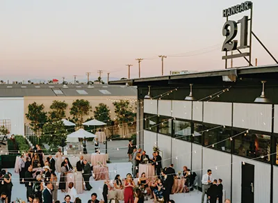 Guests gathered on the outdoor patio beneath the Hangar 21 sign at sunset.