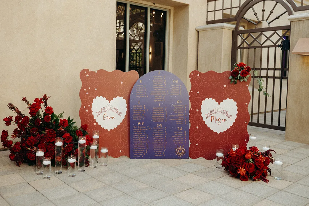 Wedding seating display with red flowers and candles beside an arched doorway.