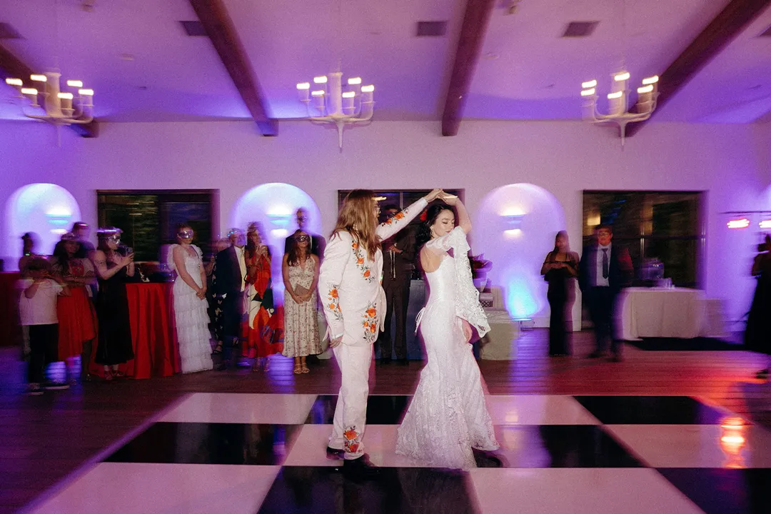 Wedding couple dancing on a checkered floor under purple reception lighting.