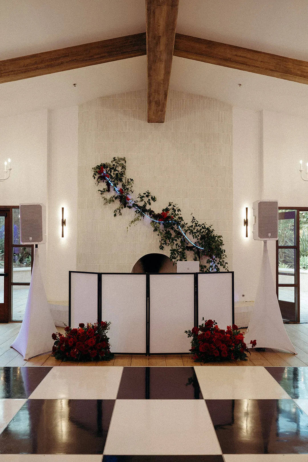 DJ booth framed by flowers and a fireplace beside a checkered dance floor.