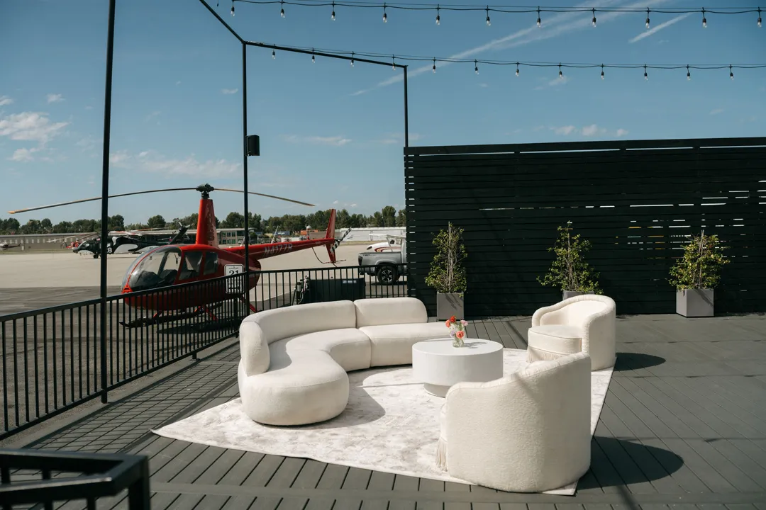 Curved white lounge seating on Hangar 21's deck with a red helicopter beyond the railing.