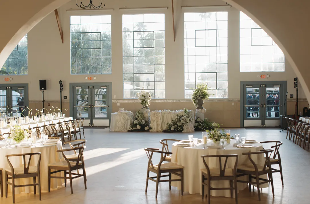 Wedding reception tables and a floral sweetheart table beneath Grand Gimeno's tall windows.