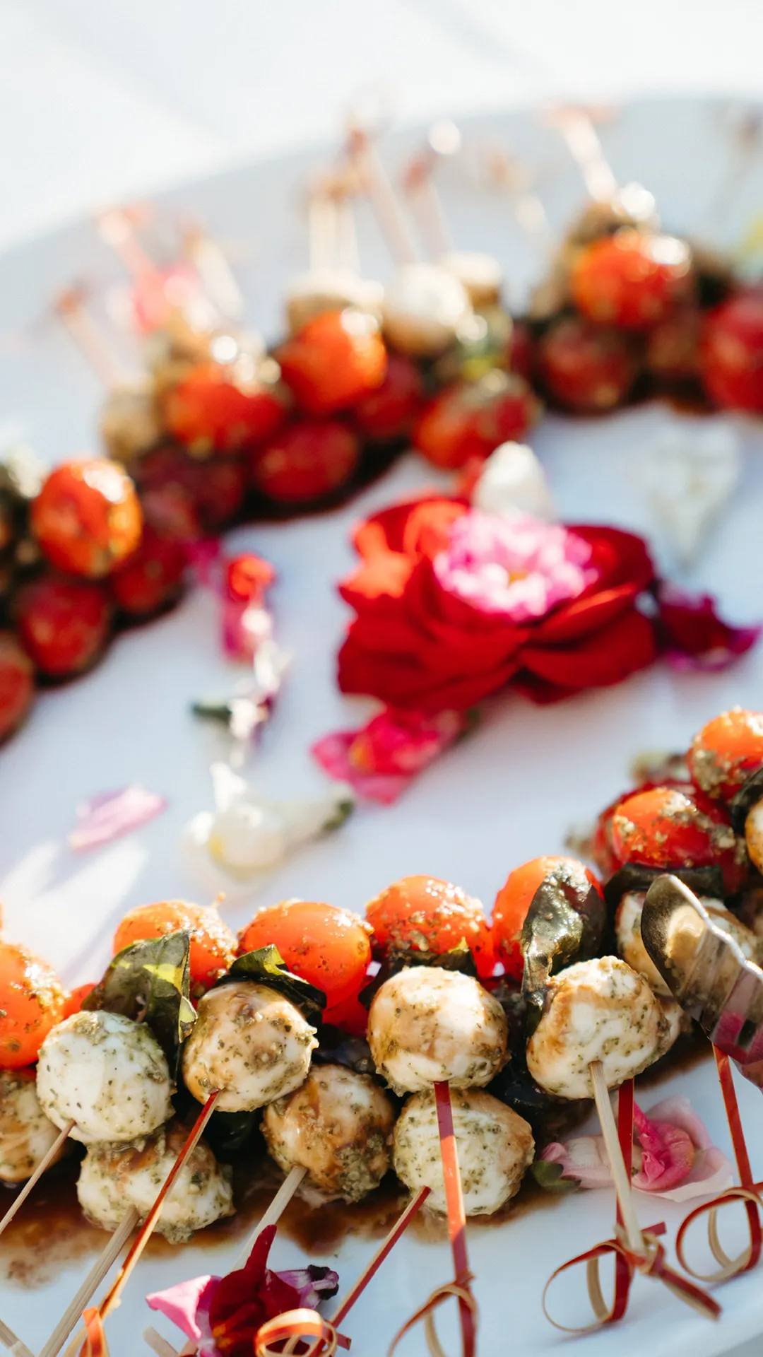 Tomato, mozzarella and basil skewers arranged around flowers on a platter.