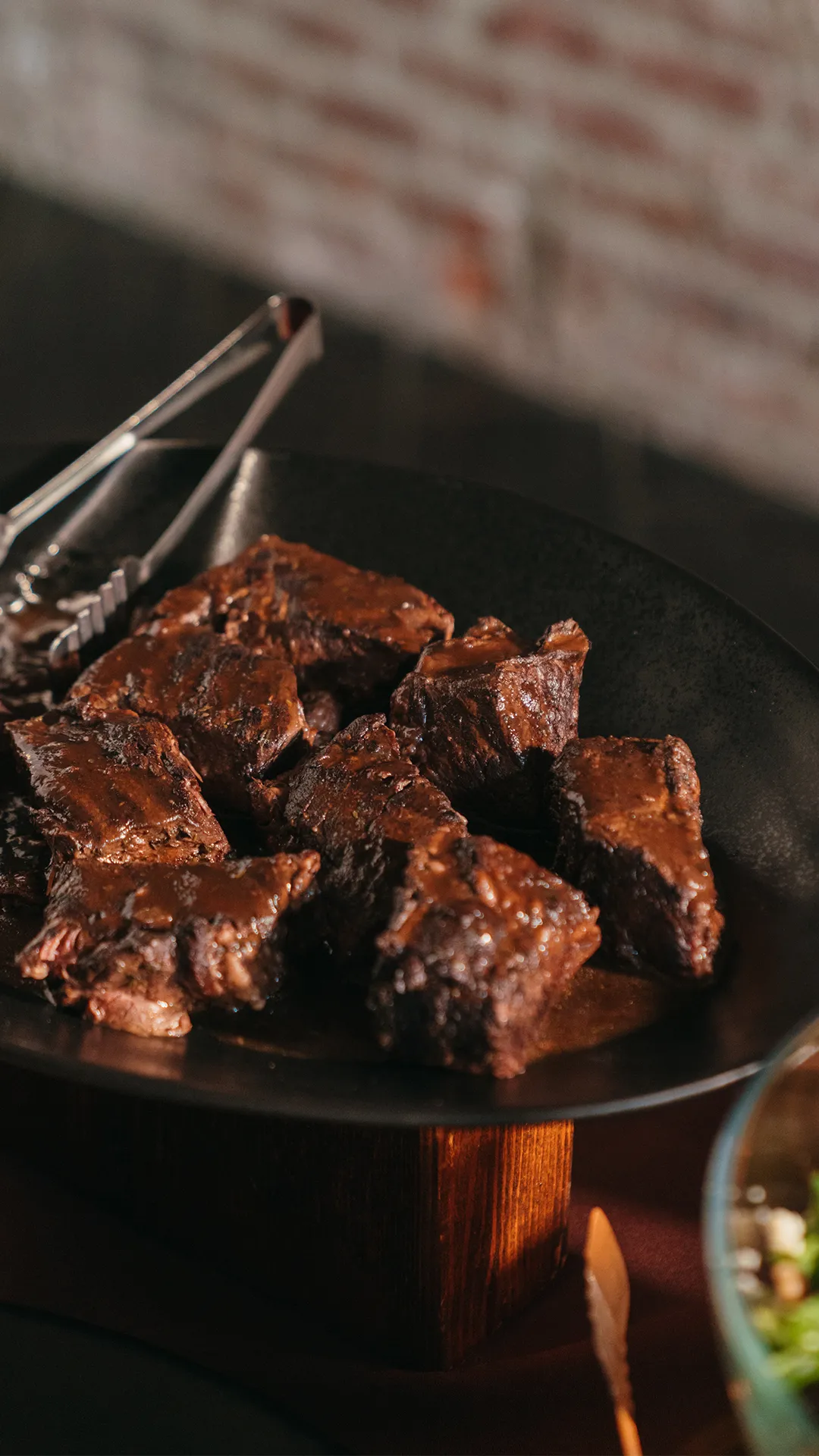 Braised short ribs in sauce on a black serving platter.