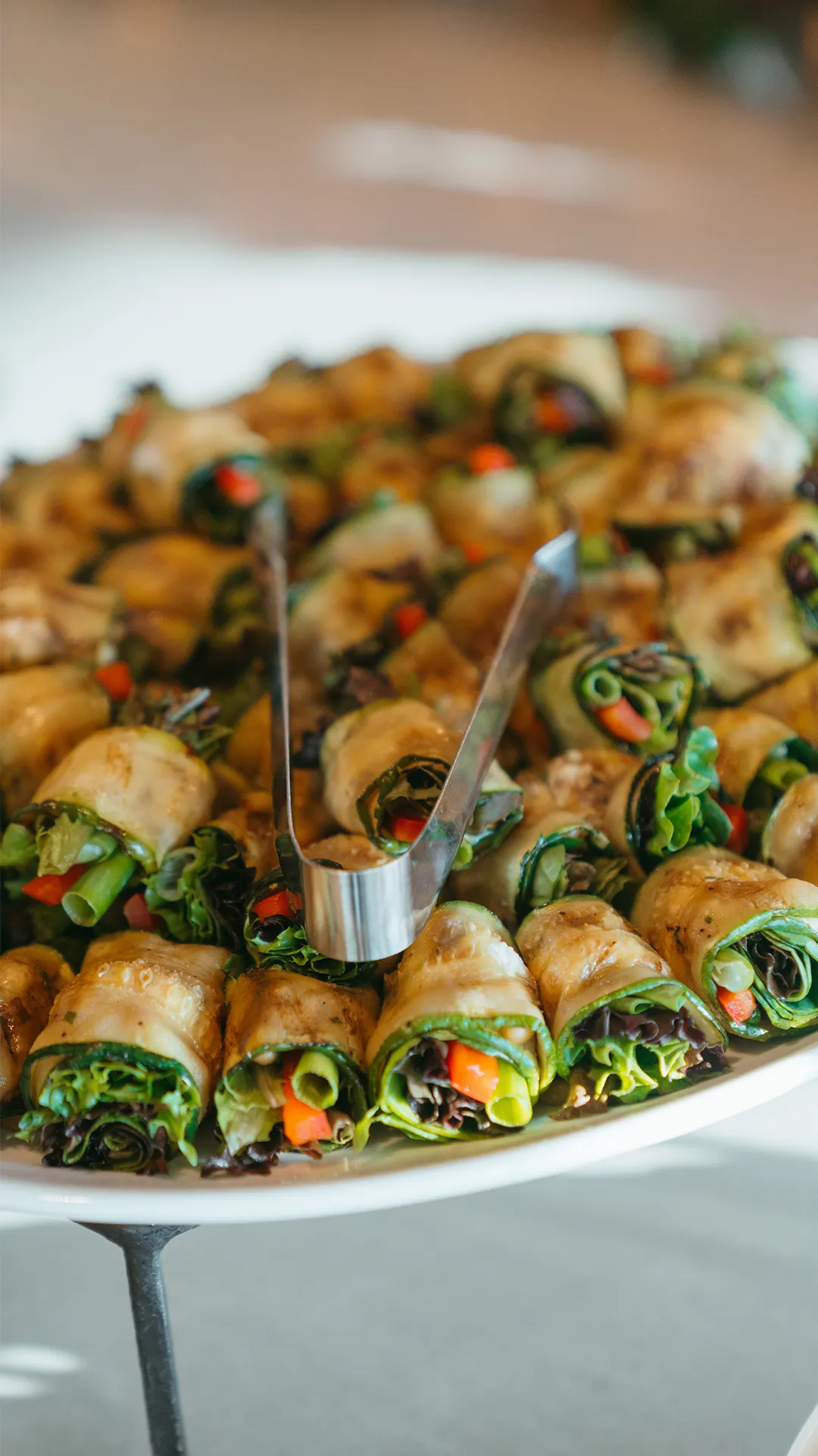 Vegetable-filled roll-ups arranged on a platter with serving tongs.