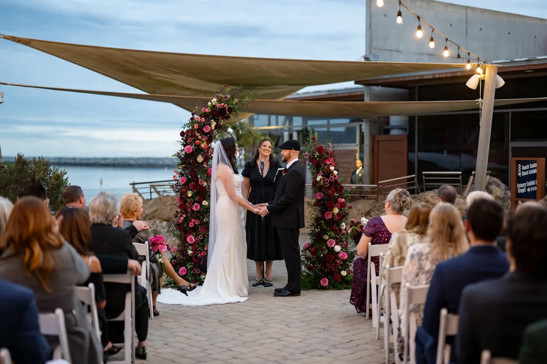 Outdoor wedding ceremony with an ocean view and plum-colored flowers.
