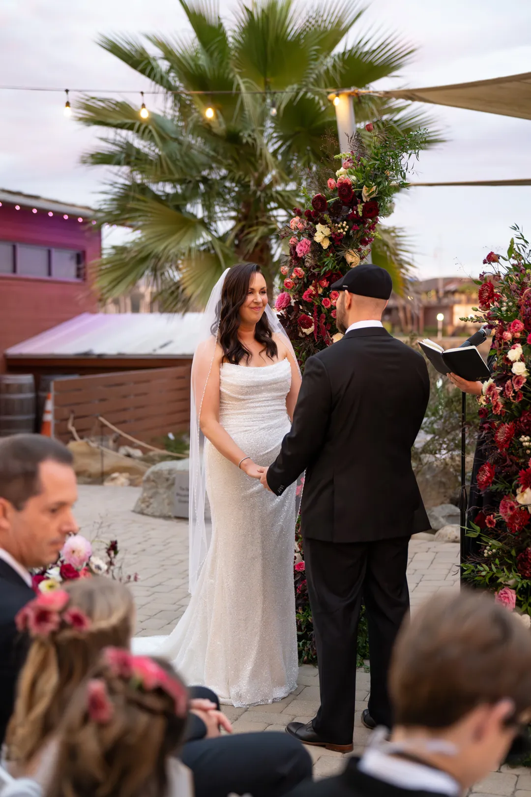 Wedding couple holding hands beneath a colorful floral ceremony arch.