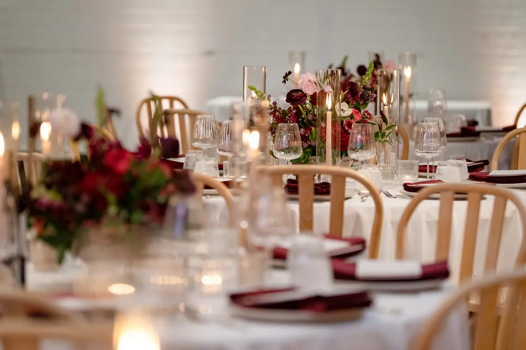 Reception table with colorful flowers, glass candles and wooden chairs.