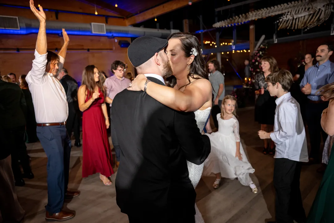 Wedding couple kissing on the dance floor surrounded by celebrating guests.