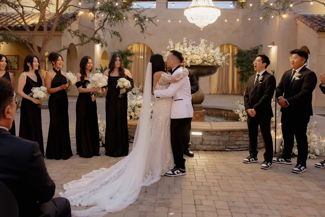 Wedding couple kissing in front of their wedding party and the courtyard fountain.