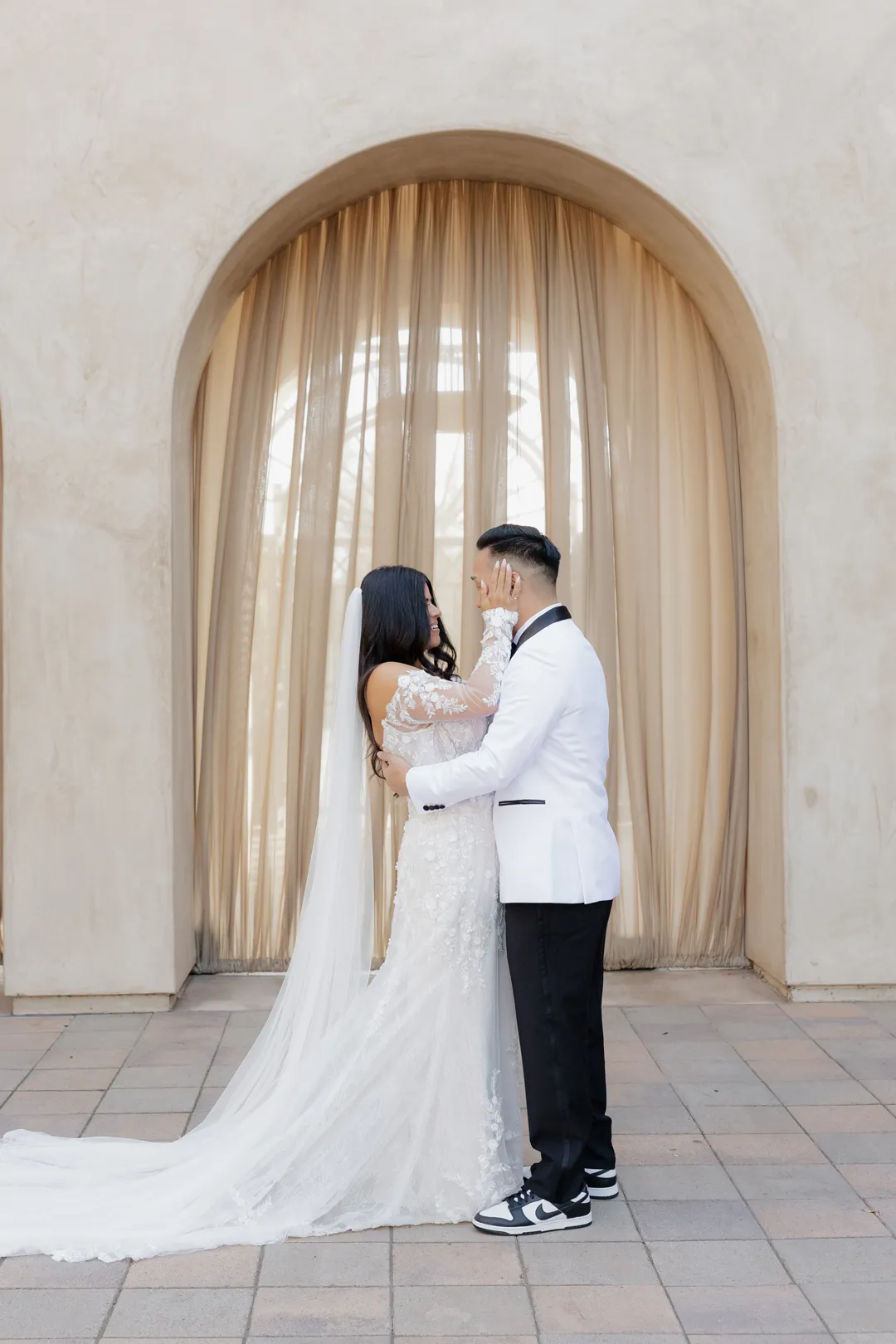 Wedding couple embracing beneath a curtained archway.