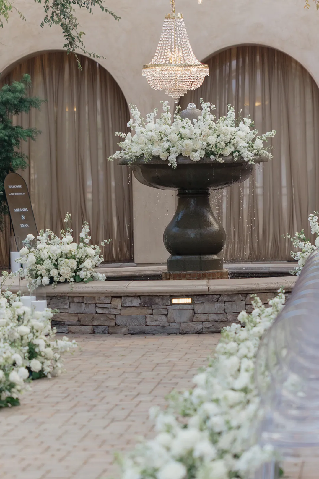 White flowers decorating a courtyard fountain beneath a crystal chandelier.