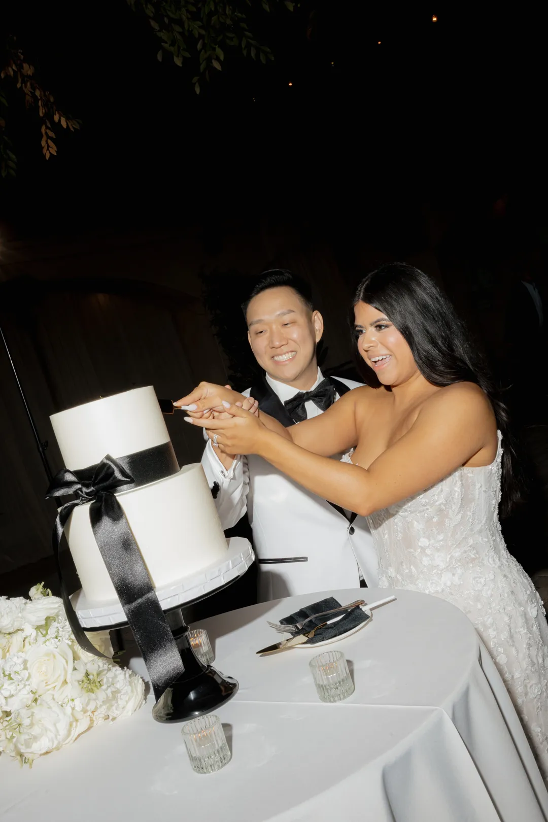 Wedding couple cutting their two-tier cake with a black ribbon.