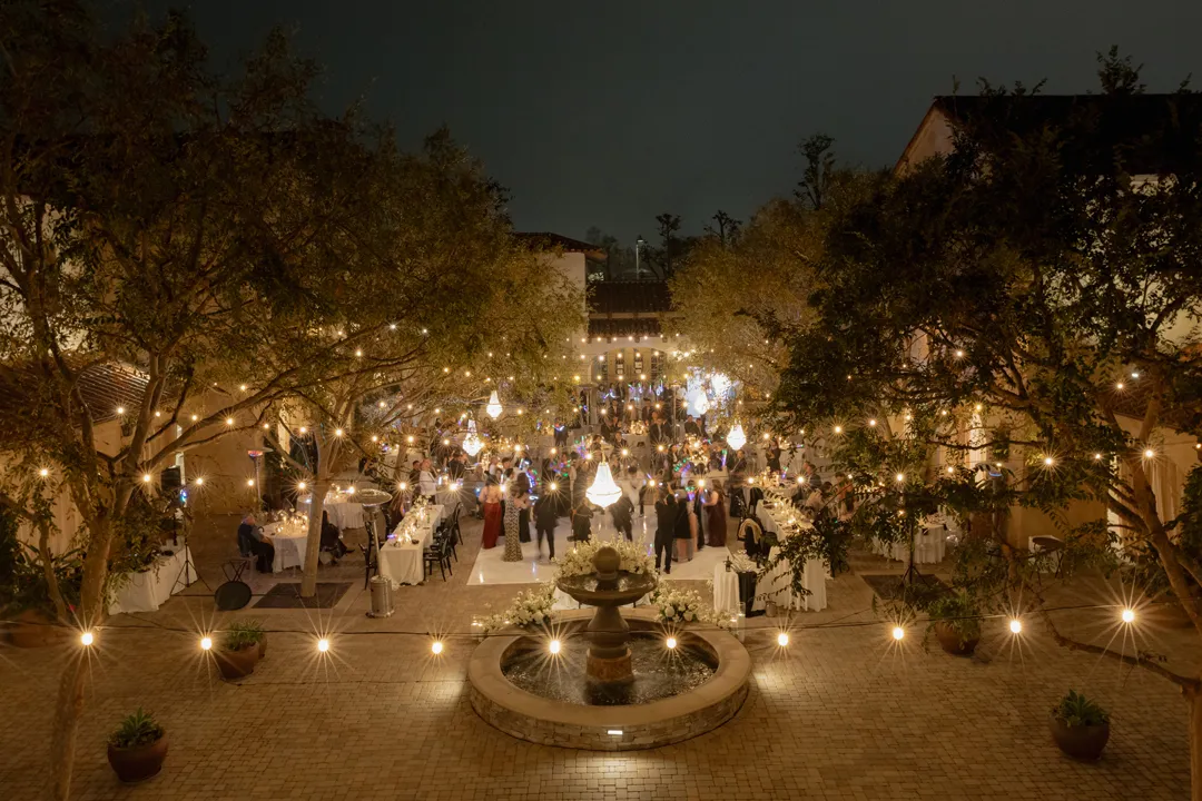 Courtyard fountain and reception tables illuminated by string lights at night.