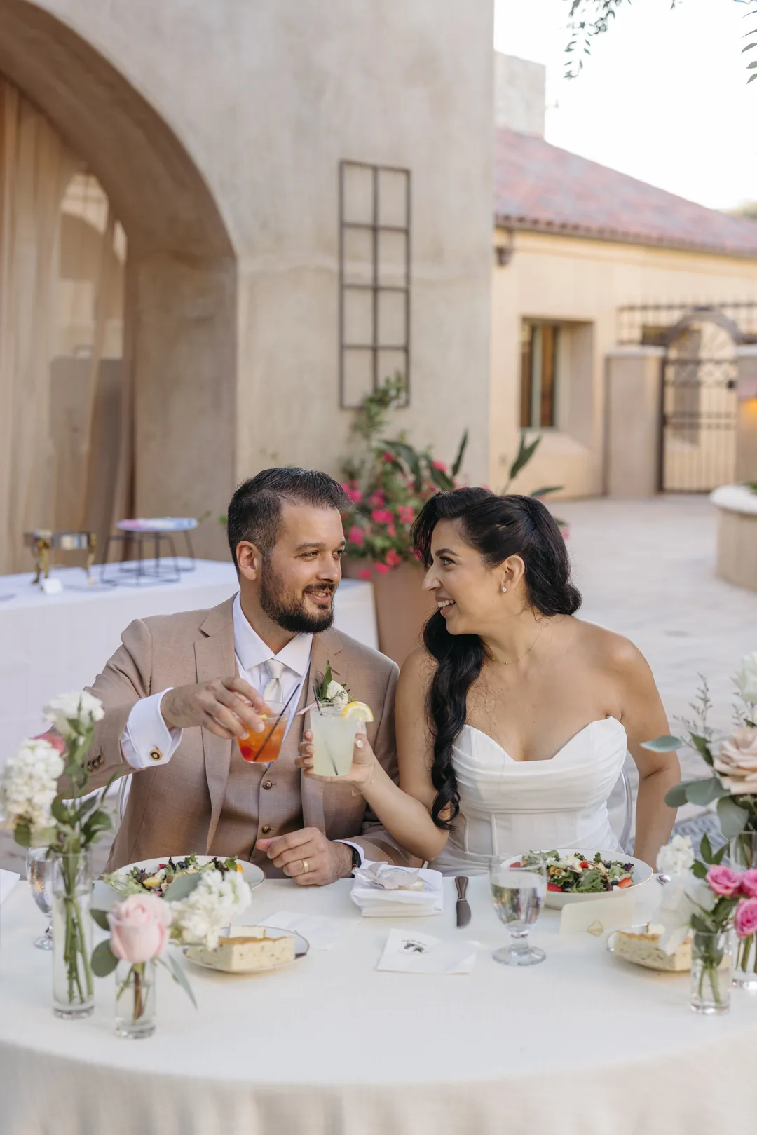 Wedding couple sharing drinks at their flower-decorated sweetheart table.