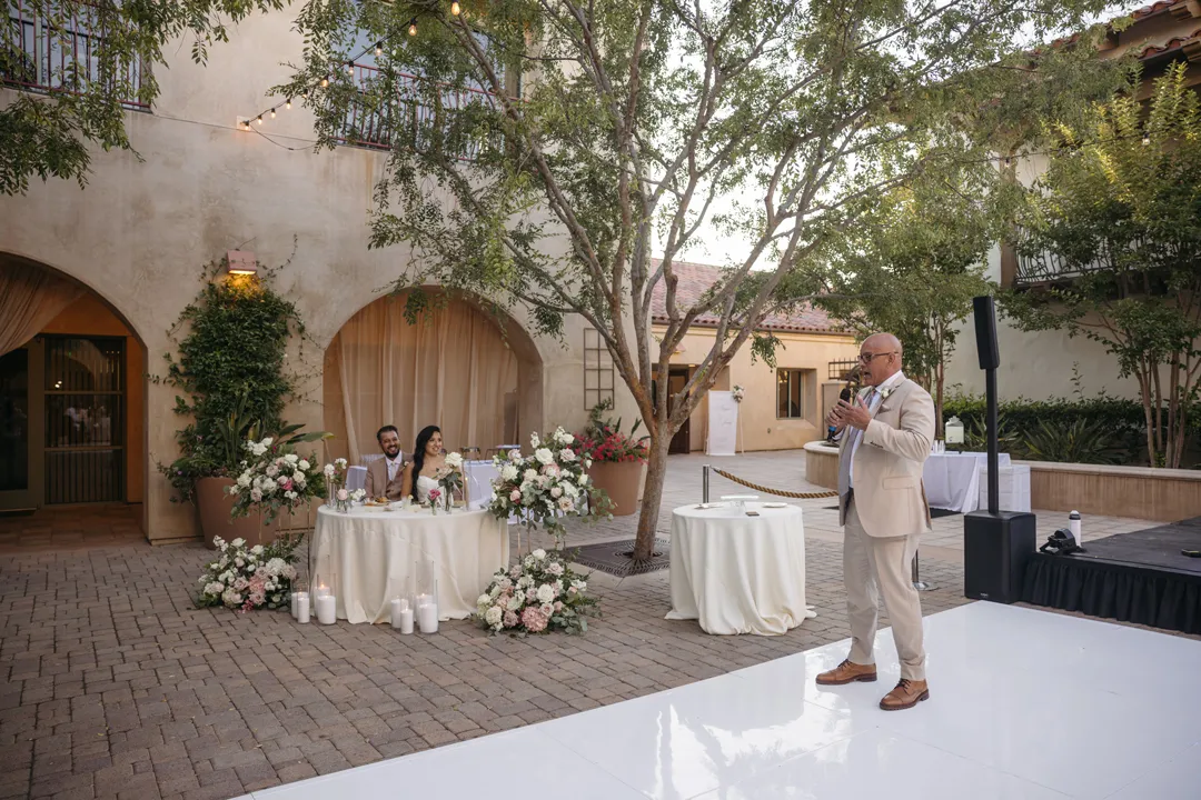 Guest giving a toast beside the courtyard sweetheart table.