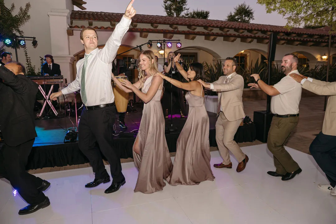 Wedding guests dancing in a line on the white dance floor.