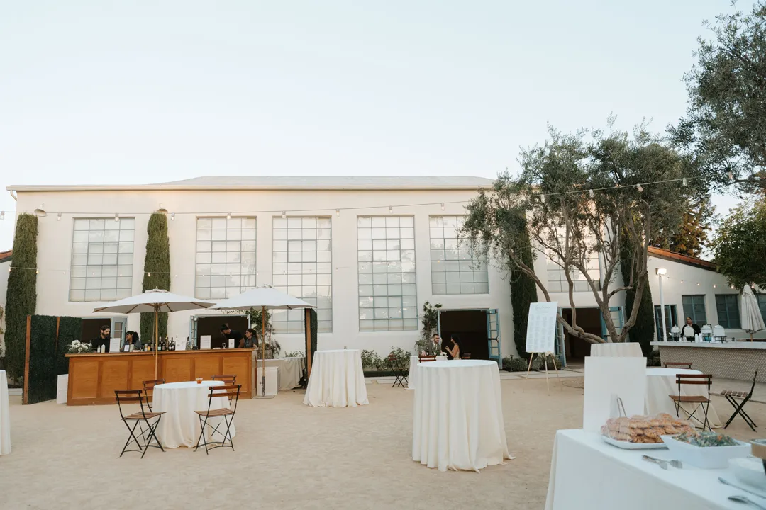 Outdoor cocktail-hour courtyard with a wooden bar, umbrellas and linen-covered tables.