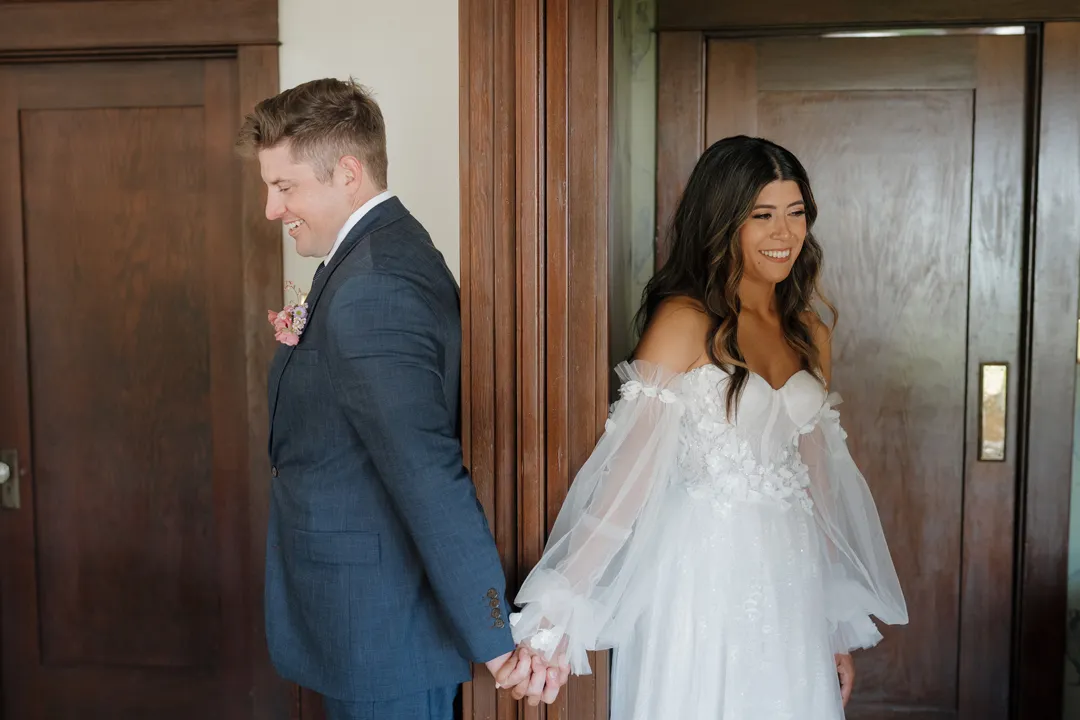 Wedding couple holding hands around a wooden doorway before their first look.