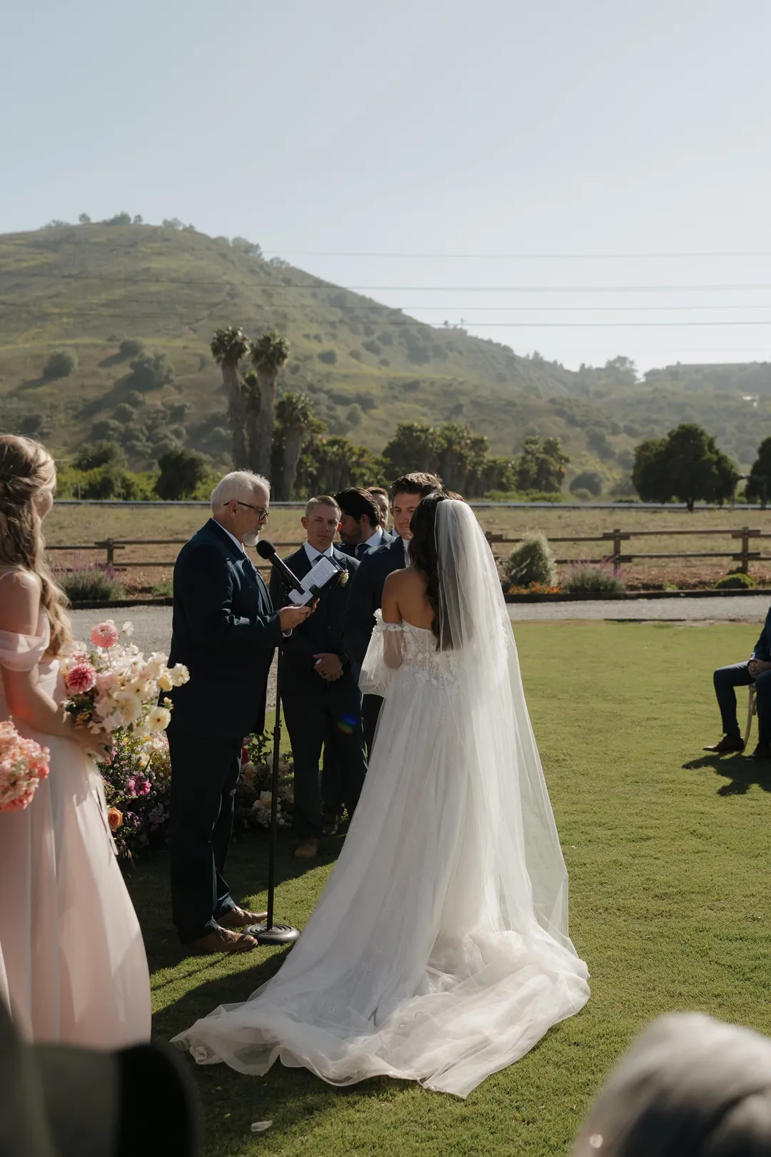 Wedding couple exchanging vows with green hills behind them.
