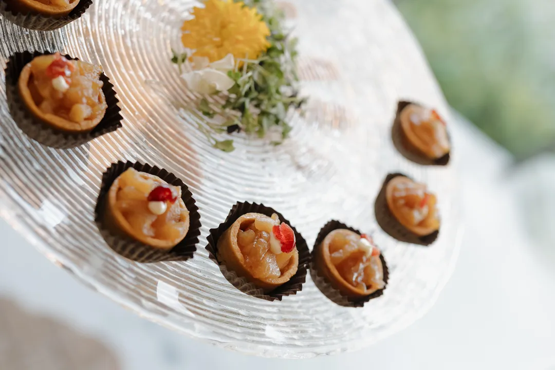 Bite-sized tartlets arranged on a clear glass serving platter.