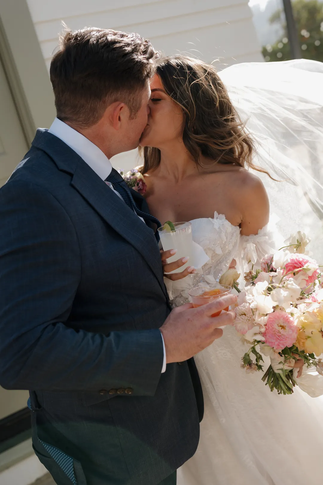 Close-up of the wedding couple kissing beside a pastel bouquet.