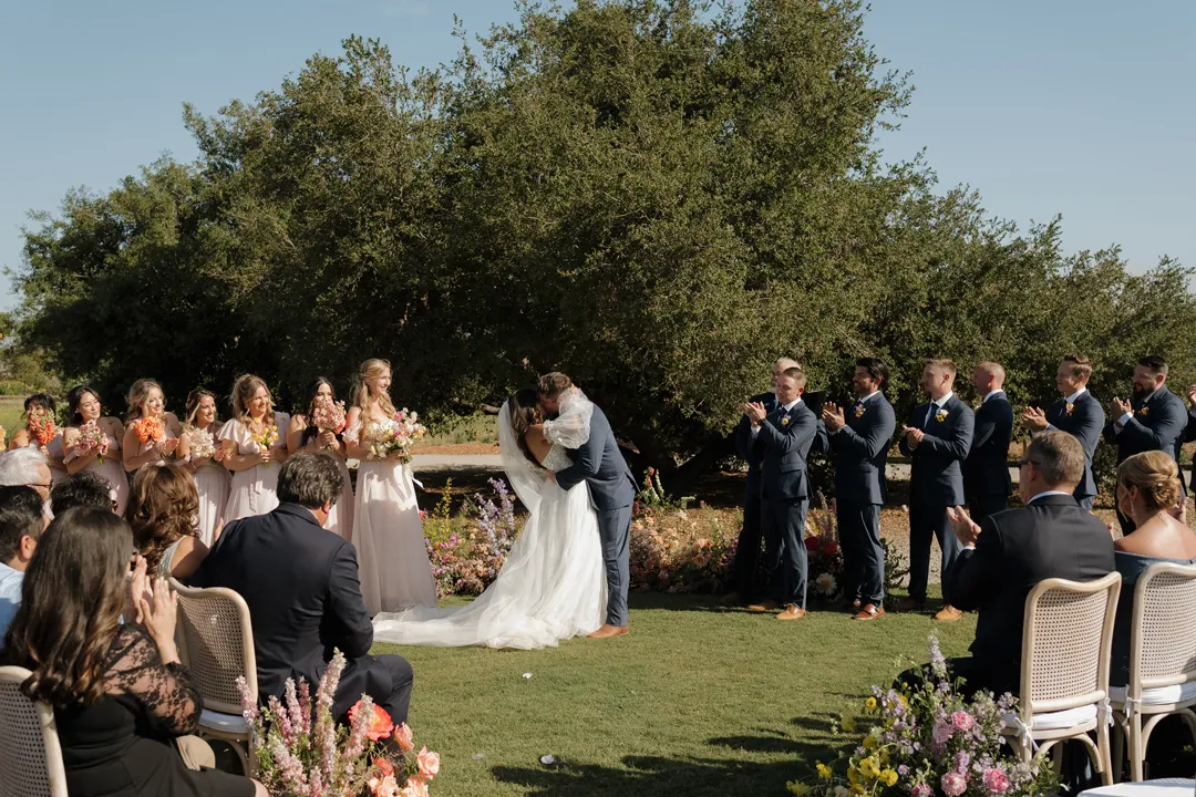 Newlyweds kissing as their wedding party applauds.