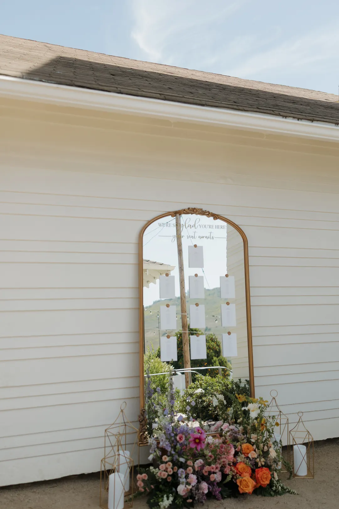 Gold-framed mirrored seating display decorated with flowers beside a white building.