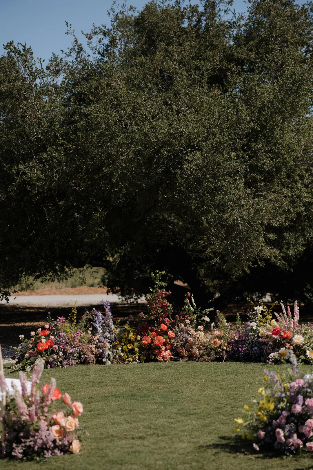 Colorful ceremony flowers arranged beneath a large tree.