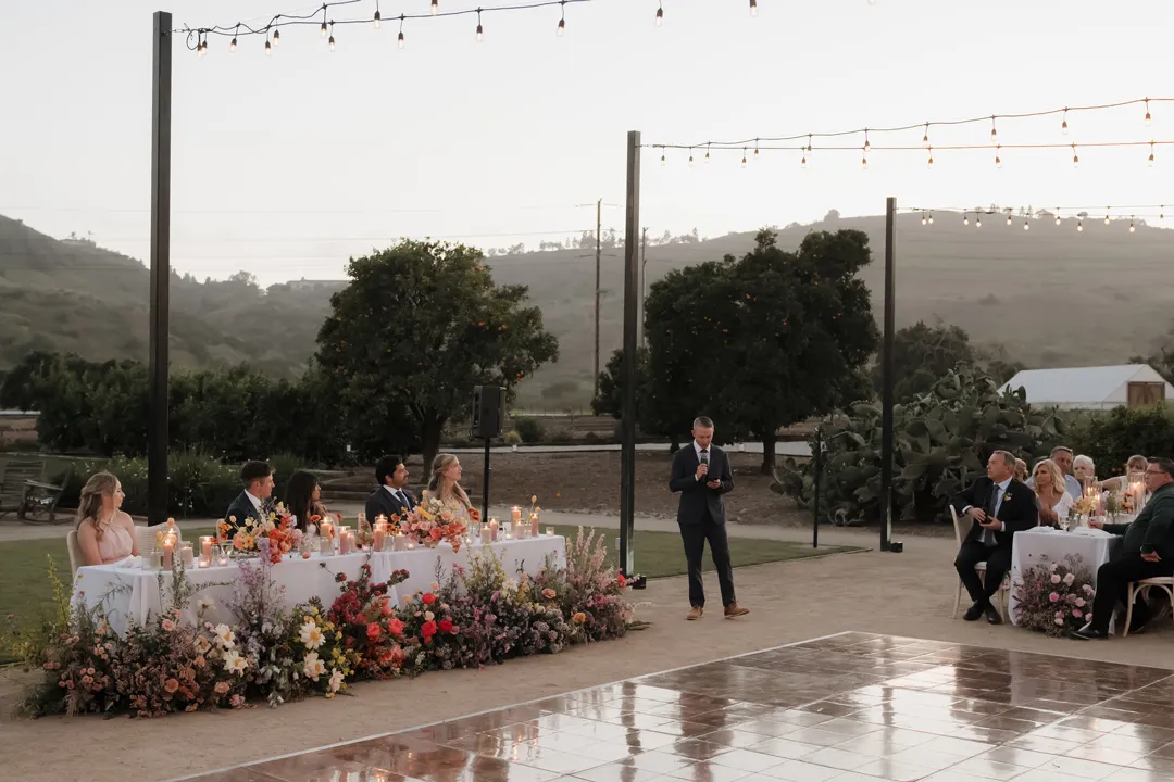 Guest giving a toast beside the flower-covered sweetheart table.