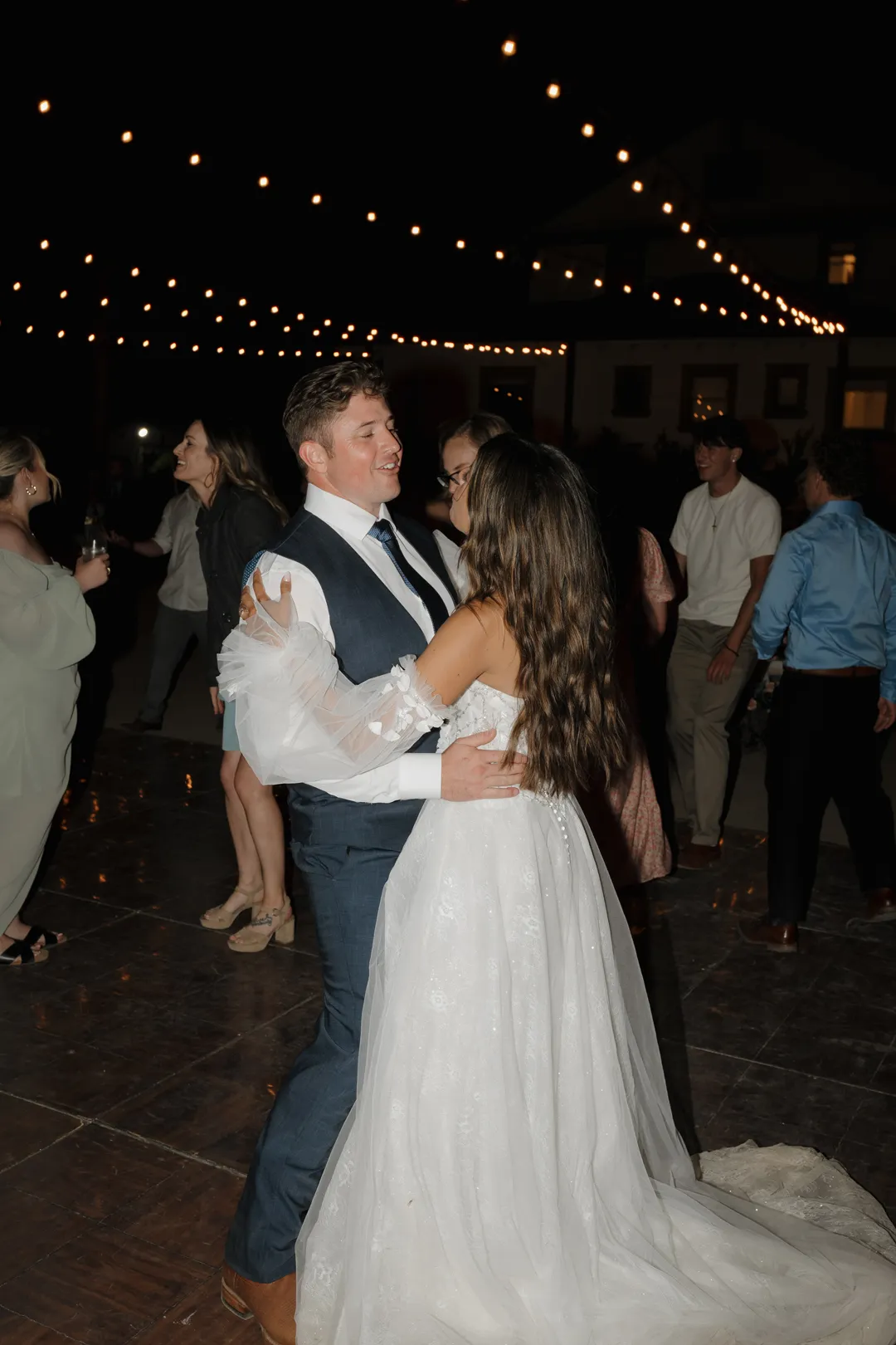 Wedding couple dancing together beneath nighttime string lights.