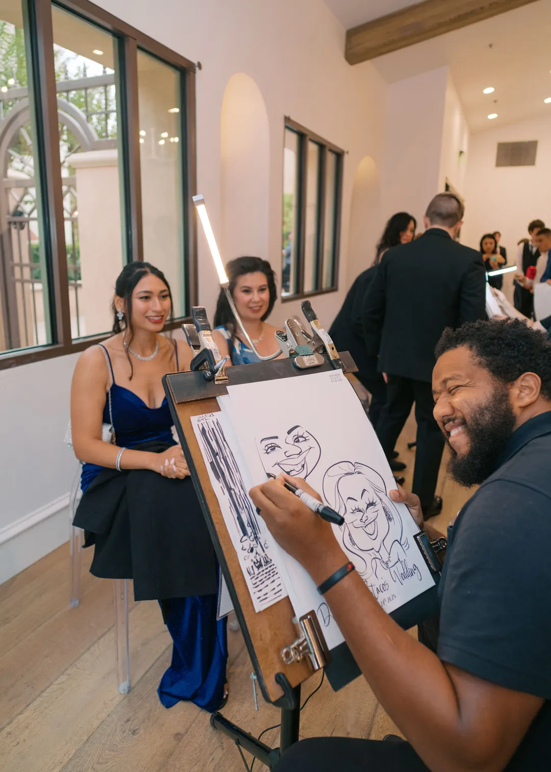 Caricature artist sketching two seated wedding guests.