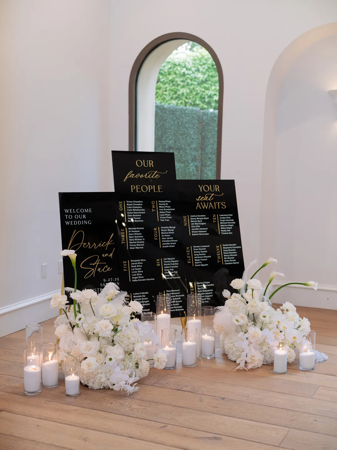 Black and gold wedding seating signs surrounded by white flowers and candles.