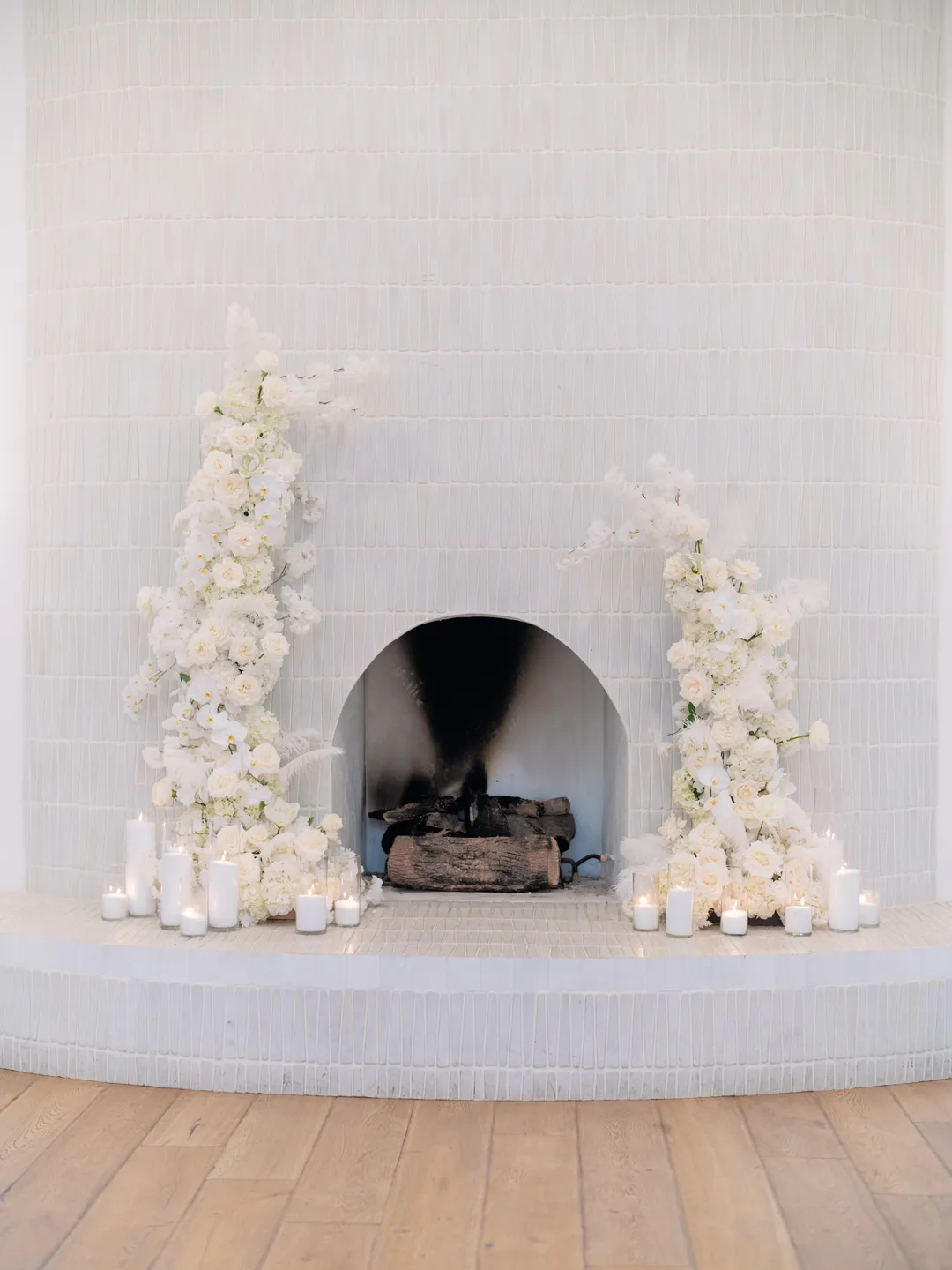 White-tiled fireplace decorated with white flowers and candles.