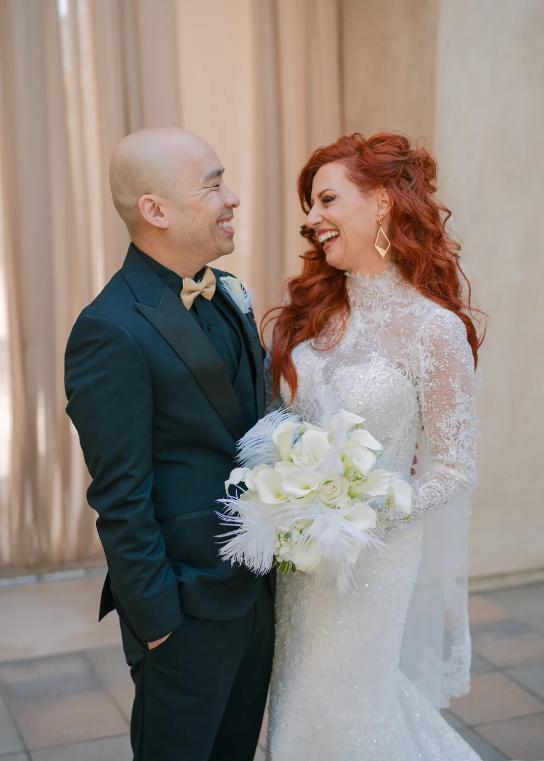 Wedding couple smiling together with a white floral and feather bouquet.