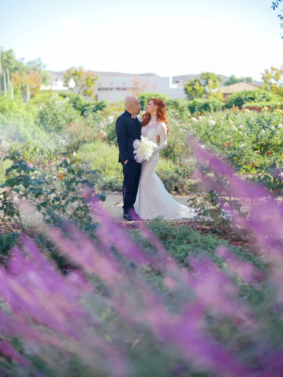 Wedding couple kissing in a garden framed by purple flowers.