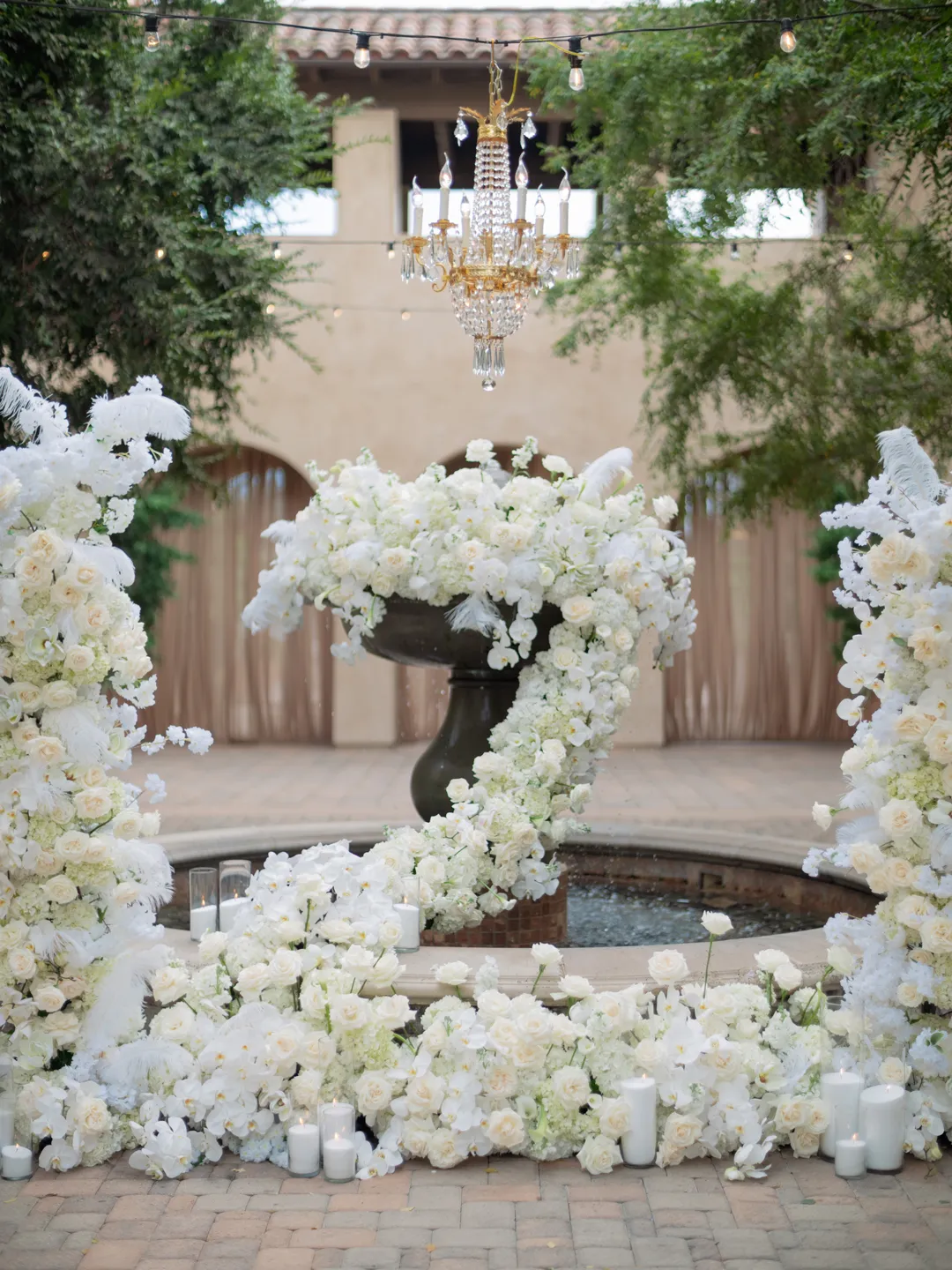 Courtyard fountain surrounded by cascading white flowers and candles.