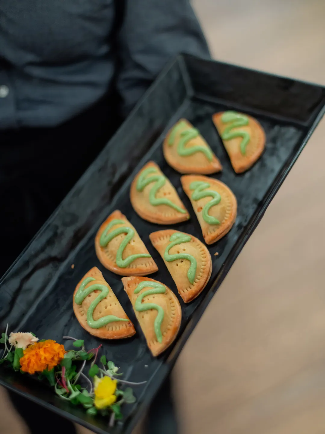 Tray of golden half-moon pastries topped with green sauce.