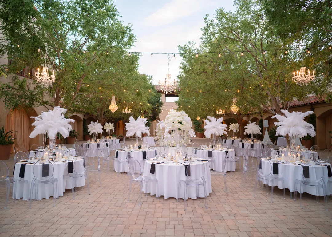 Courtyard reception tables with tall white feather centerpieces beneath chandeliers.