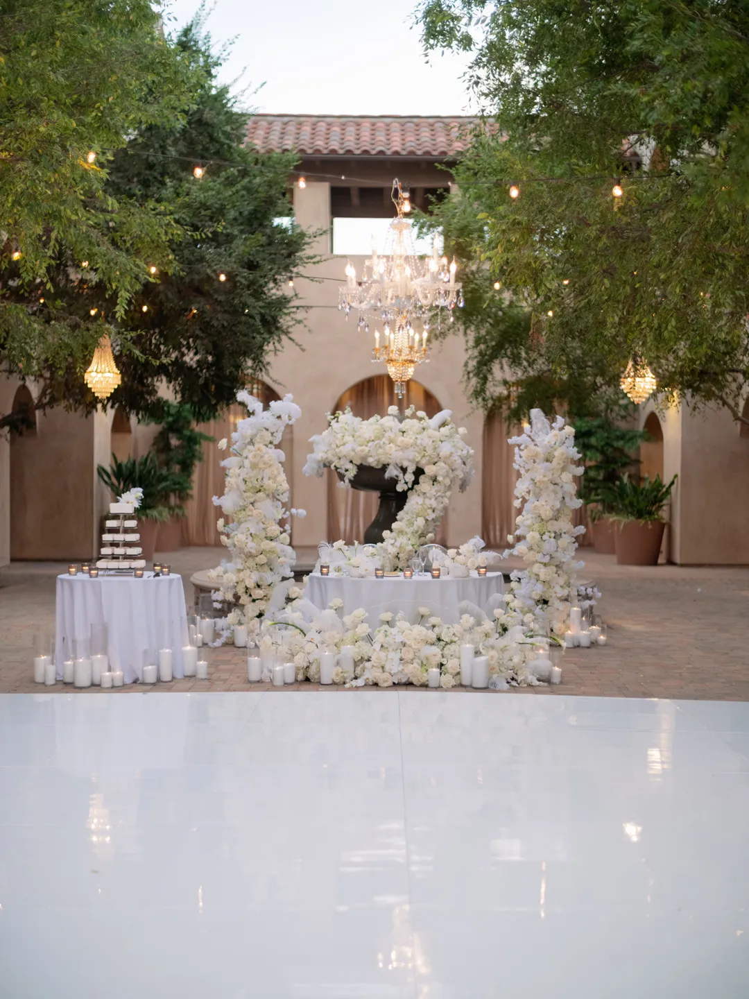 White dance floor and flower-covered fountain beneath courtyard chandeliers.
