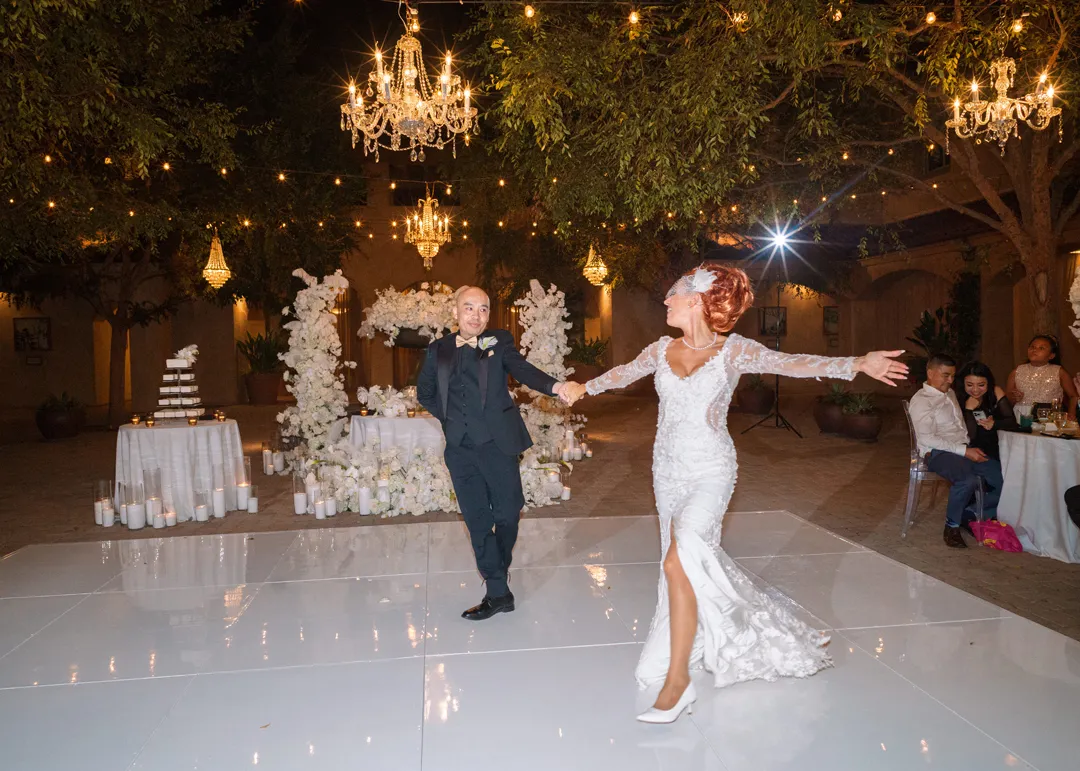 Wedding couple dancing across the white floor beneath evening chandeliers.